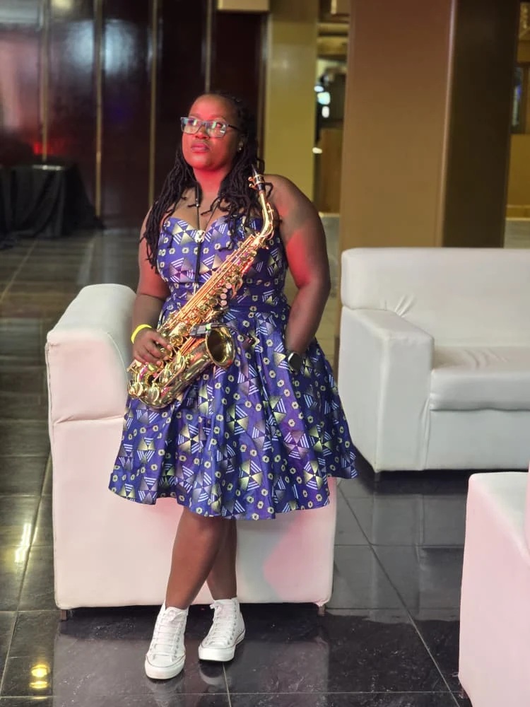 Tina Watyoka with saxophone in a blue patterned dress