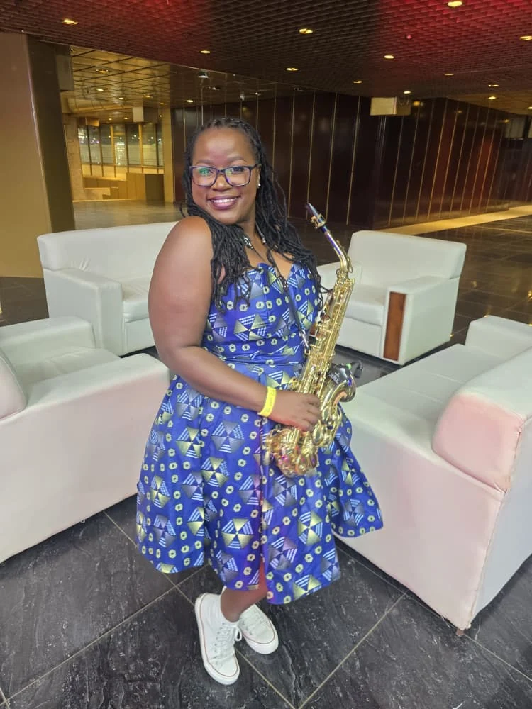 Tina Watyoka with saxophone in a blue patterned dress