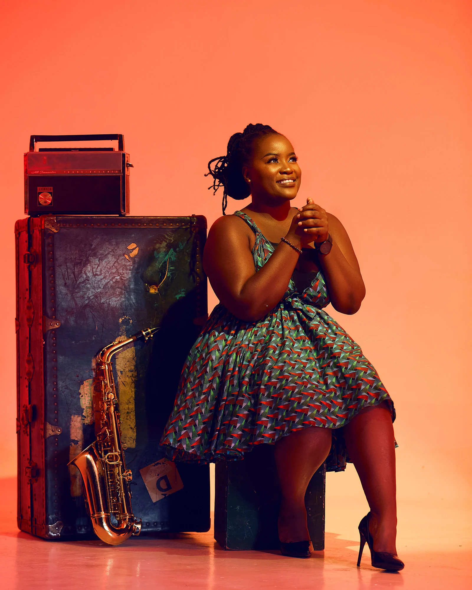 Tina Watyoka seated beside her saxophone against an orange backdrop
