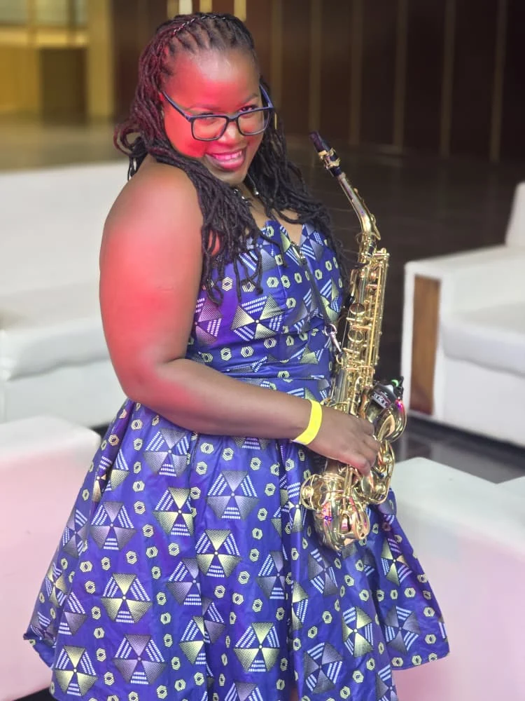 Tina Watyoka with saxophone in a blue patterned dress