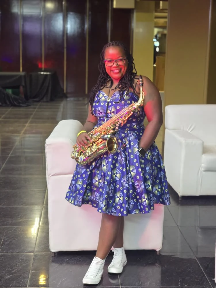 Tina Watyoka with saxophone in a blue patterned dress
